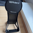 Černý elektronický bicí pad na kovovém stojanu. Na horní části jsou bílé nápisy Roland a V-Drums. Povrch padu i stojanu je v dobrém stavu bez viditel…