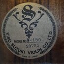 Fotografie detailu vnitřní štítku nástroje z dřeva. Na kulatém štítku je nápis KISO SUZUKI VIOLIN CO., LTD. a MADE IN JAPAN. Je zde uveden MODEL NO.…