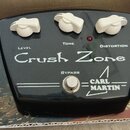 Černý kytarový efekt s bílými ovládacími knoflíky. Na horní straně jsou nápisy LEVEL, TONE a DISTORTION, uprostřed velký nápis Crush Zone a v dolní č…