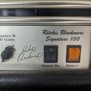 Detailní pohled na ovládací panel kytarového zesilovače stříbrné barvy. Na panelu je nápis „Ritchie Blackmore Signature 100“ a pod ním podpis „Ritchi…