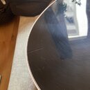 Detailní záběr na černý, lesklý povrch hudebního nástroje s bílým okrajem. Na černé ploše jsou viditelné jemné škrábance a otřepy. Žádné značky ani n…