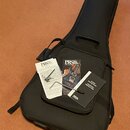 Černý polotvrdý pouzdro na kytaru. Na pouzdře leží dokumentace s nápisy PRS Paul Reed Smith GUITARS a GUITAR DESCRIPTIONS & OPERATING INSTRUCTIONS. V…