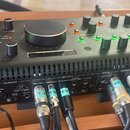 Černý stolní audio mixér značky behringer. Na horním panelu jsou ovládací knofíky, tlačítka a velký centrální ovratový regulátor. Zadní panel obsahuj…