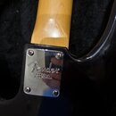 Detail krku a těla elektrické kytary v černé barvě. Na kovém krytu spojení krku s tělem je vyryto logo Fender a nápis CORONA, CALIFORNIA. Povrch laku…
