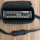 Černý digitální mixér v černé přepravní tašce s popruhem. Na zadním panelu jsou viditelné nápisy REMOTE, ETHERNET, CLIENT, MIDI, USB a MAIN L, MAIN R…