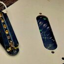 Bílá kytarová pickguard s dvěma prázdnými oválnými otvory a jedním instalovaným černým humbuckerem. Snímač má zlaté póly a je připojen bílým a černým…