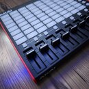 Černý MIDI kontrolér s bílými podsvícenými pady a řadou posuvníků. Na zařízení jsou viditelná loga AKAI PROFESSIONAL a nápisy VOLUME, PAN, FADER CTRL…