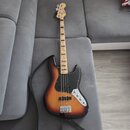Elektrická basová kytara s korpusem v barevném přechodu od žluté přes oranžovou k červené a černé. Nástroj má černý pickguard, stříbrný most a ladící…