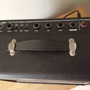 Černý kytarový kombo zesilovač s koženým povrchem a úchytem. Na ovládacím panelu je nápis ANALOG MODELING AMPLIFIER a logo VTONE GM110. Panel obsahuj…