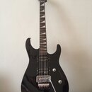 Černá elektrická kytara s dvojstupňovitým úhlem hlavy a hrotovými polohovými značkami na hmatníku. Na těle jsou dva humbuckery, ovládací knoflíky a t…