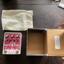 Na fotografii je efekt pedál bílé barvy s červeným grafickým motivem, textilní vak a otevřená kartonová krabice. Na pedálu je nápis Astral Destiny a…