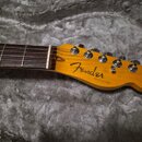 Fotografie zachycuje hmatník a hlavu elektrické kytary v přirozené dřevěné barvě. Na hlavě je čitelné logo Fender a pod ním nápis TELECASTER. Nástroj…