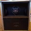 Zadní pohled na kytarový reproduktor v hliníkovém flightcase s černým vnitřkem. Na reproduktoru je vidět nápis BLACK SHADOW a logo MESA/BOOGIE. Ve sp…