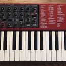 Červený syntetizátor s klaviaturou. Na pravé straně je bílý nápis „nord lead 4 performance synthesizer“. Horní panel obsahuje množství černých ovrato…