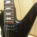 Detail elektrické kytary v černé barvě s hnědým hmatníkem a bílými hranatými polohovými značkami. Je vidět jeden černý humbucker s viditelnými polosl…