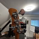 Fotografie zachycuje hlavu basové kytary z přírodního dřeva s четыřmi chromovanými ladičkami. Na zadní straně hlavy je vidět štítek s nápisy „CE“, „M…