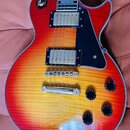 Elektrická kytara s trupem v červeno-žlutém sunburst provedení a viditnou strukturou dřeva. Nástroj má dva humbuckery s kovovými kryty, černý pickgua…