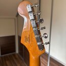 Zadní strana hlavy kytary v přírodním dřevě s chromovanými ladičkami. Na zadní straně hlavy je nápis: Designed and Rocked by Fender s číslem s/n ISB2…