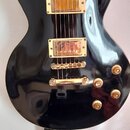 Černá elektrická kytara s gold hardwarem a hnědým hmatníkem. Na těle jsou dva humbuckery, čtyři otočné knofíky a přepínač s nápisy RHYTHM a TREBLE. P…