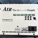 Zadní strana bílého akustického zesilovače v černém rámu. Na horní části je nápis AER The Acoustic People® a níže označení Compact 60₃ twin channel a…