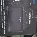 Černý kartonový obal kytarového zesilovače s nápisem Guitar Amplifier KATANA-MINI a logem BOSS. Na krabici je bílý symbol meče a text KATANA - Japane…