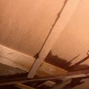 Detailní pohled do vnitřku dřevěného nástroje. Jsou vidět světlé dřevěné lišty a povrch s výraznými tmavými skvrnami, které připomínají zbytky lepidl…