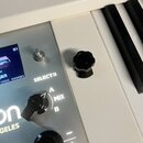 Detailní záběr na ovládací panel bílého klávesového nástroje s kovovým povrchem. Jsou vidět nápisy SELECT B, MIX A a B, část loga s textem GELES a oz…