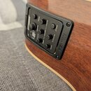 Detailní záběr na elektroniku akustické kytary s hnědým dřevěným povrchem. Černý ovládací panel obsahuje nápisy FISHMAN, tuner, volume, bass, middle,…