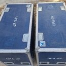 Dvě modré transportní bedny s kovými hranami a madly. Na horní i boční straně obou beden je bílý nápis UPA-2P. Na bednách jsou viditelné nálepky s lo…