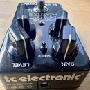 Černý efekt pedál značky tc electronic. Na horní straně jsou čtyři černé oválné ovladače a jeden přepínač, s popisky LEVEL, VOICE a GAIN. Ve spodní č…