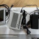 Sada elektronického příslušenství značky RTW položená na bílém kartonu s nápisem Monitor TM3. Soubor obsahuje stříbrný displej s logem RTW, stříbrnou…