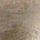 Detailní pohled na povrch mosazného činele s viditelným opracováním v podobě koncentrických rýh. Na povrchu je vyryto logo PAISTE a sériové číslo 644…