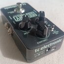 Černý efekt pedál značky tc electronic s nápisem SENTRY. Na horní straně jsou dva černé ovládací knoflíky s popisky DECAY a THRESHOLD, stoupací spína…