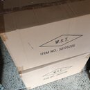 Fotografie zobrazuje tři hnědé cardboardové krabice naskládané na sebe. Na dvou spodních krabicích je černý potisk s logem W.S.T. v kosočtverci a náp…