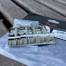 Krom chromovaného mostu pro basovou kytaru je na fotografii vidět balení s nápisem Fender a sáček s montážními šrouby. Na štítku balení je uveden tex…