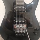 Černá elektrická kytara s dvěma humbuckery a chromovaným tremolo mostem. Na mostě je viditelný nápis GOTOH MADE IN JAPAN. Povrch kytary vykazuje drob…