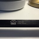Detailní záběr na černý kovový povrch s bílými nápisy. Je zde vidět logo a text TRICK DRUMS USA. Vedle nich jsou uvedeny nápisy Patent No. 7,633,000…