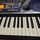 Digitální klavír značky YAMAHA, model PSR-260. Nástroj má modré ovládací panely s bílými klávesami a černými hracími klávesami. Na displeji je vidite…
