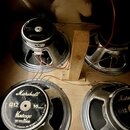 Fotografie zachycuje čtyři reproduktory v dřevěné skříni. Na zadní straně reproduktorů jsou viditelná loga Marshall a nápisy G12, 16 ohms, Vintage BY…