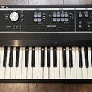 Černý digitální klavír s bílými a černými klávesami. Na ovládacím panelu jsou nápisy Roland V-Combo, sekce PIANO, SYNTH a DRUM, knoflíky, tlačítka a…