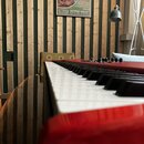 Detailní pohled na klávesnici červeného elektronického nástroje. Jsou vidět bílé a černé klávesy a část ovládacího panelu s několika černými knoflíky…