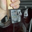 Detail krku a těla elektrické kytary s tmavě červeným lakem. Na kovové spojovacídesce je vyryto logo Michael Kelly guitar Co. Povrch lakovaného těla…