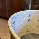 Detailní pohled do vnitřku korpusu bicího nástroje. Vnitřek je vyložen šedým, texturovaným materiálem, ve kterém jsou rozmístěny kovové šrouby. Povrc…