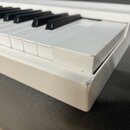 Detailní pohled na pravou část bílého digitálního klavíru s černými klávesami. Na pravém horním rohu šasi jsou viditelné odřesy a opotřebení bílého l…