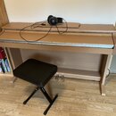 Digitální piano v dřevěněm korpusu s přezeleným povrchem a bílo-černou klaviaturou. Na horní desce nástroje leží černá sluchátka s připojeným kabelem…