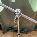 Detail chromovaného mechanismu s úchvatem na kovovém stojanu. Horní část tvoří vodorovná tyč s texturovaným, světle šedým povrchem. Na kovových částe…