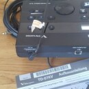 Černý elektronický bicí modul značky Roland V-Drums. Na horní hraně je nápis DRUM SOUND MODULE TD-07 a na spodní straně jsou popisky vstupů DC IN, US…