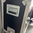 Černý transportní case s hliníkovými hranami a kovovými rohy. Na boku je umístěna kovová rukojeť s černým úchopem a v dolní části kovový zámek. V pra…