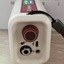 Bílé plastové zařízení s červeným oválným knoflíkem. Na spodní části jsou umístěny tři konektory: vstup pro kytaru, USB port a výstup pro sluchátka,…