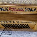 Akordeon v béžové barvě s modrými ornamentálními vzory. Na přední části je červený nápis ROYAL STANDARD. Nástroj vykazuje známky opotřebení v podobě…